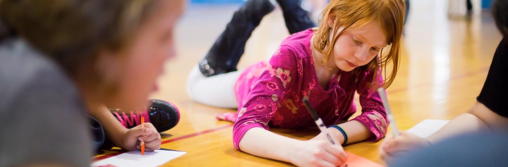 A Young Girl Writing on A Gym Floor