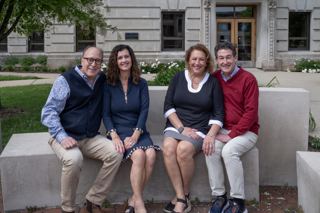 Kevin and Beth Theile & Amanda and John Burnham seated on a stone bench in front of the Monroe County Courthouse